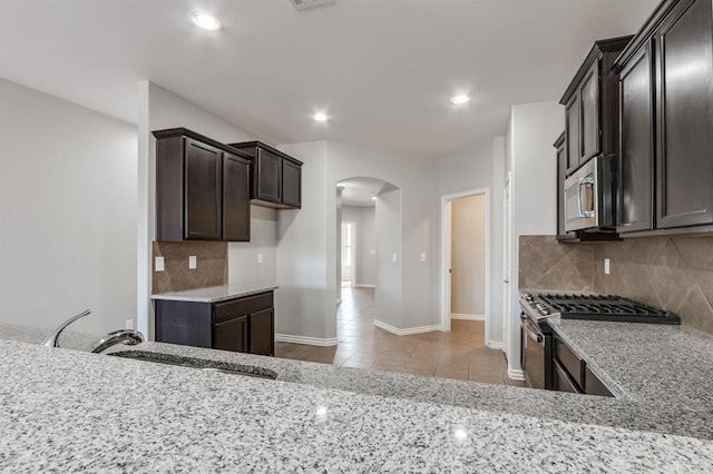 kitchen with appliances with stainless steel finishes, sink, backsplash, light tile patterned floors, and light stone countertops