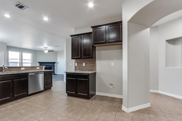 kitchen featuring sink, backsplash, light stone counters, dark brown cabinetry, and stainless steel dishwasher