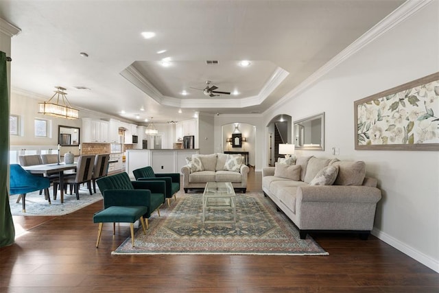 living room featuring a tray ceiling, dark wood-type flooring, ornamental molding, and ceiling fan