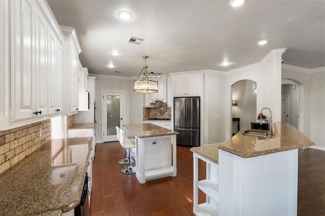 kitchen featuring sink, stainless steel fridge, white cabinets, a kitchen island, and dark stone counters