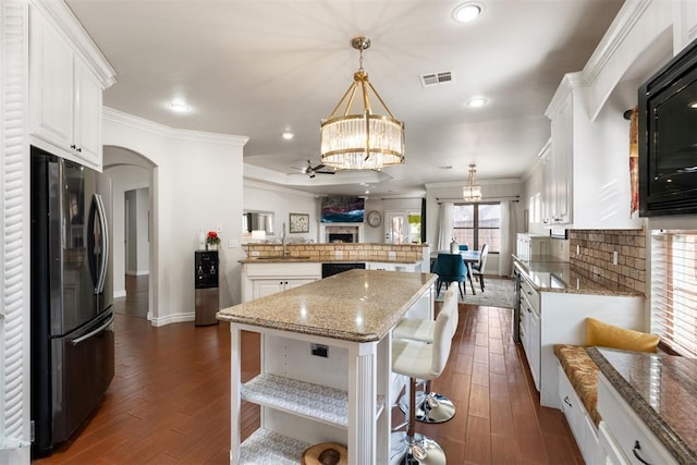 kitchen featuring a breakfast bar, black fridge, white cabinetry, a center island, and hanging light fixtures