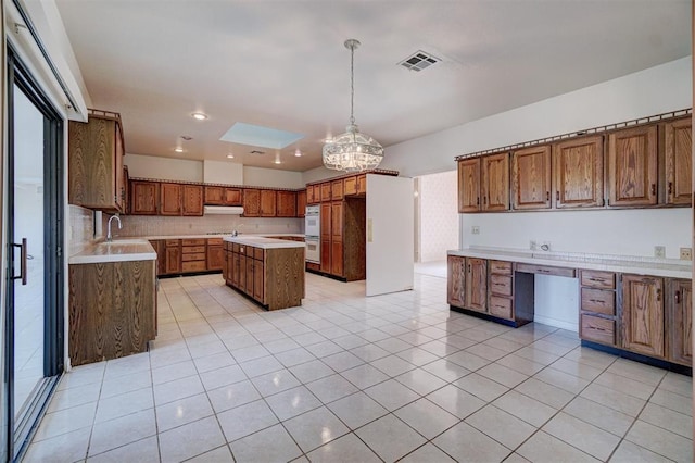 kitchen featuring sink, a center island, built in desk, light tile patterned floors, and pendant lighting