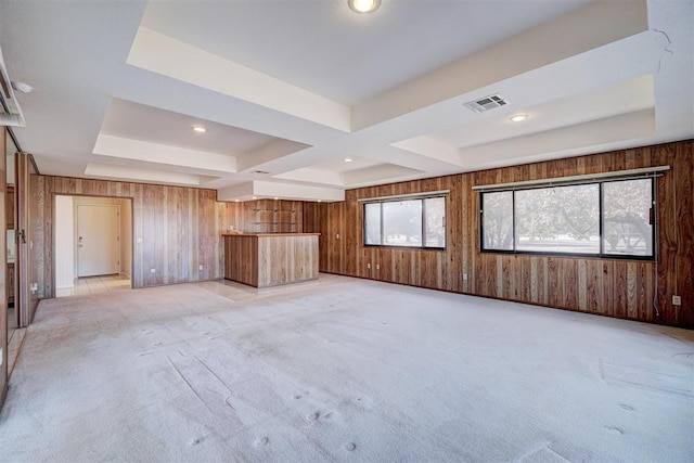 unfurnished living room with a wealth of natural light, light carpet, wood walls, and a tray ceiling