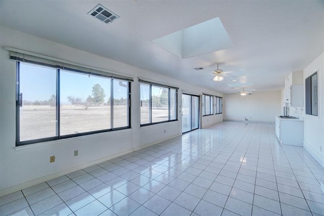 tiled empty room featuring ceiling fan, a skylight, and sink