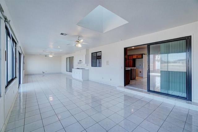 unfurnished living room with light tile patterned flooring, ceiling fan, and a skylight