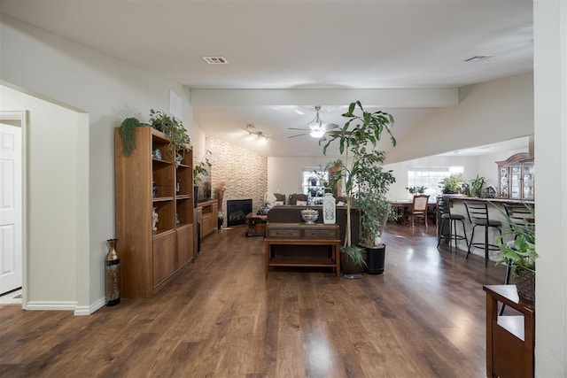 living room featuring dark wood-type flooring, ceiling fan, a fireplace, and vaulted ceiling with beams