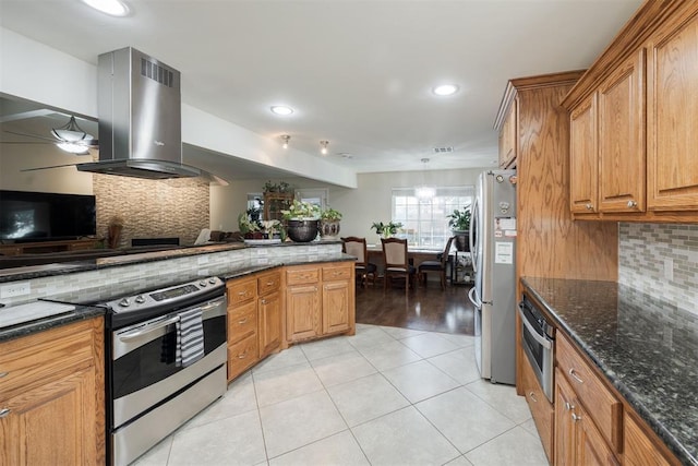 kitchen featuring light tile patterned flooring, island range hood, appliances with stainless steel finishes, dark stone counters, and decorative backsplash