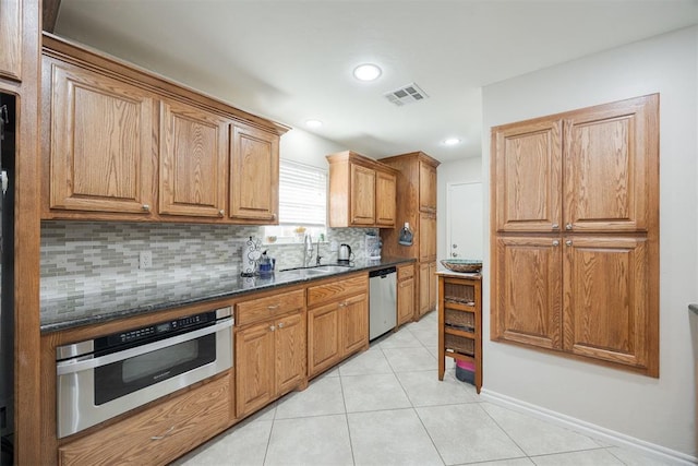 kitchen featuring light tile patterned flooring, sink, dark stone counters, stainless steel appliances, and backsplash