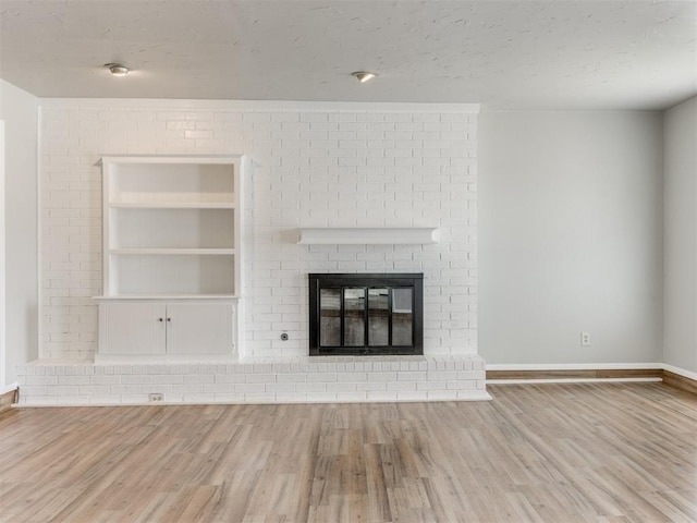 unfurnished living room featuring built in features, a fireplace, light hardwood / wood-style floors, and a textured ceiling