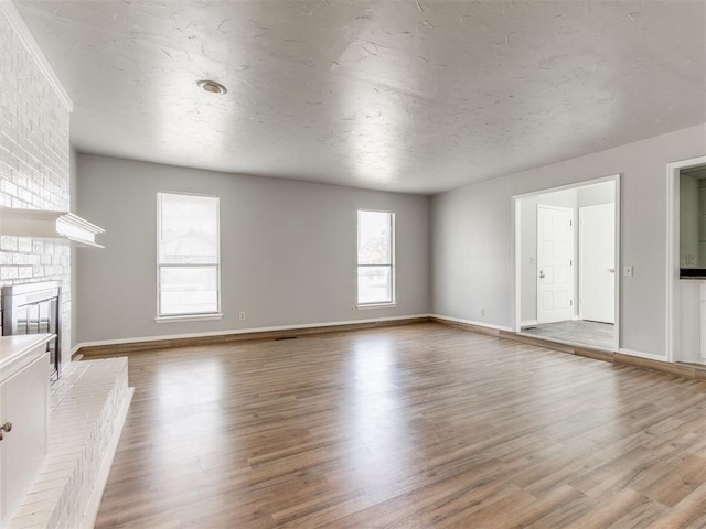 unfurnished living room with a textured ceiling, a brick fireplace, and light wood-type flooring