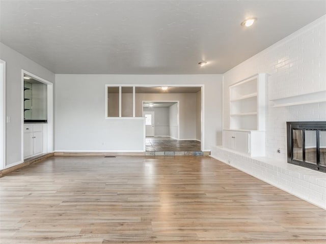 unfurnished living room featuring a brick fireplace, built in features, and light wood-type flooring