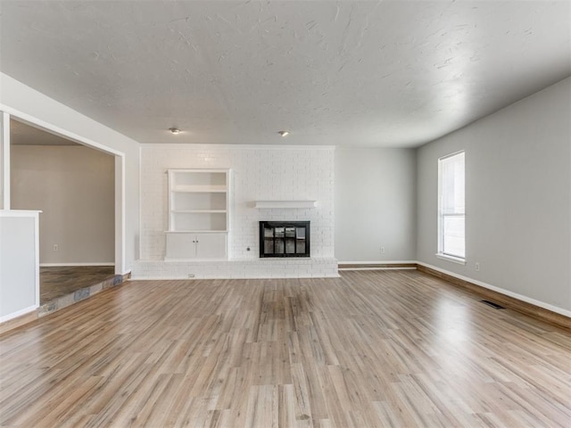 unfurnished living room featuring built in shelves, a fireplace, a textured ceiling, and light wood-type flooring