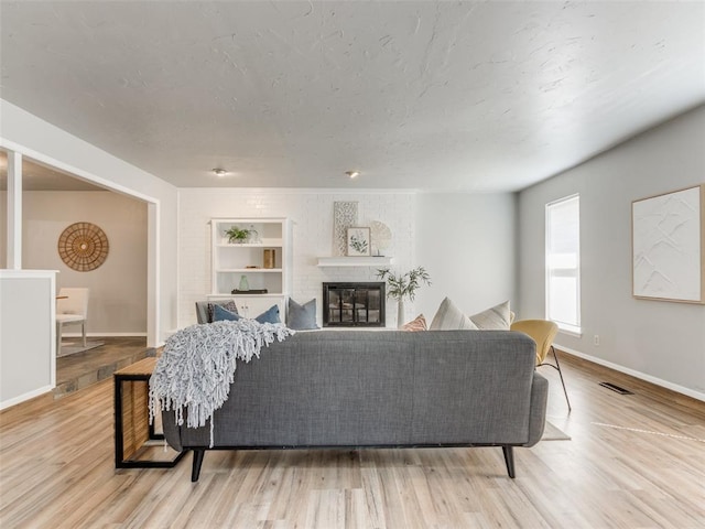 living area with visible vents, a fireplace, a textured ceiling, and wood finished floors