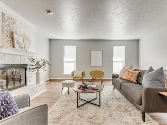 living area with a brick fireplace, wood finished floors, baseboards, and a textured ceiling