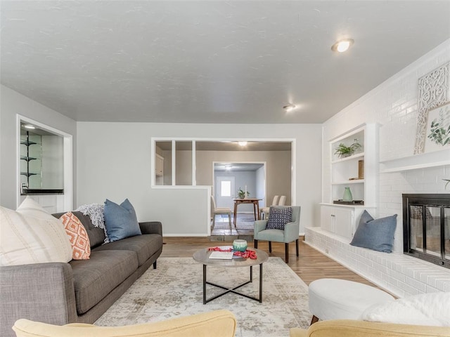 living area with built in features, a brick fireplace, baseboards, and wood finished floors