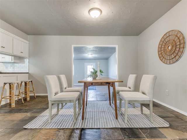 dining room featuring stone tile floors, baseboards, and a textured ceiling