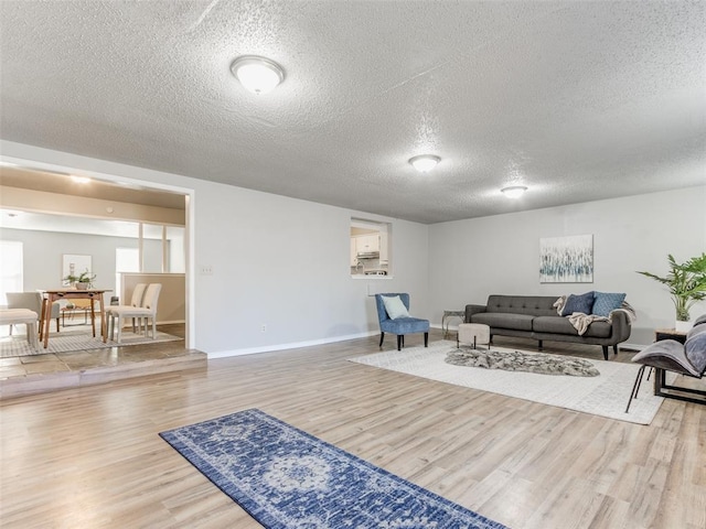 living area featuring light wood-style flooring, a textured ceiling, and baseboards