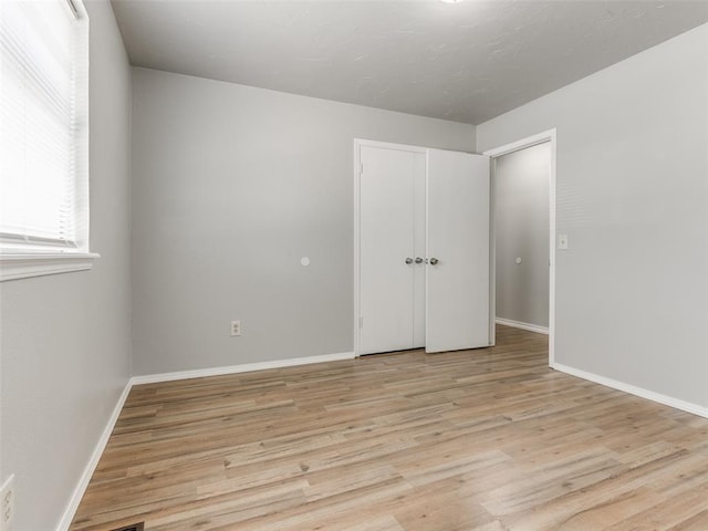 unfurnished bedroom featuring light wood-style flooring, baseboards, and a closet