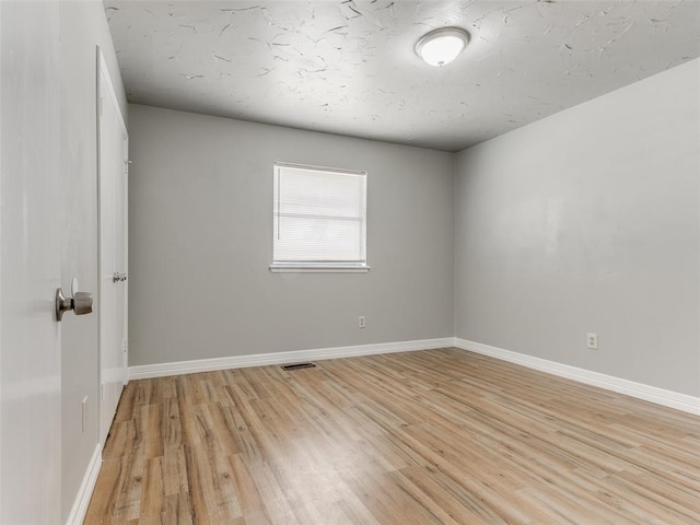 spare room featuring light wood-style floors, visible vents, and baseboards