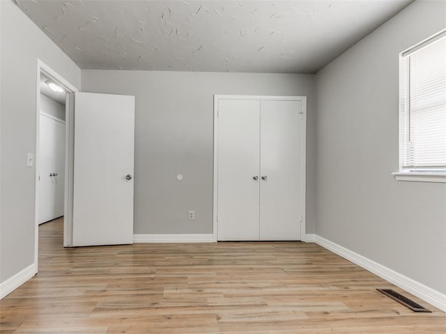 unfurnished bedroom with a closet, visible vents, baseboards, and light wood finished floors