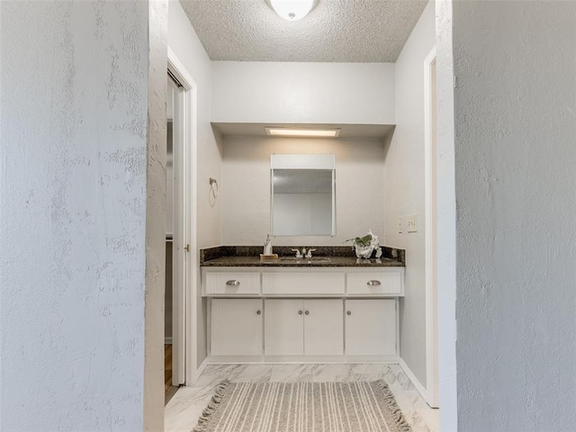 bathroom featuring vanity, a textured wall, marble finish floor, and a textured ceiling