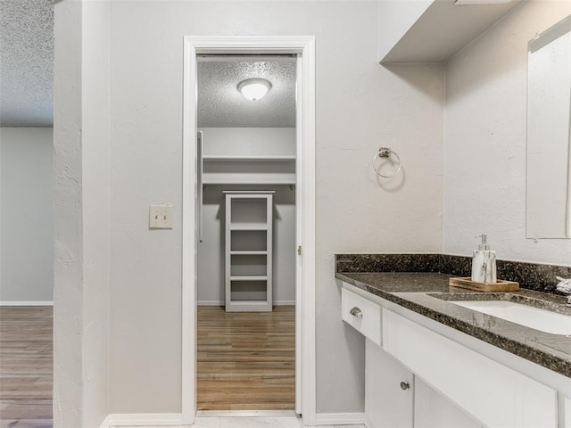 bathroom with vanity, wood finished floors, baseboards, a spacious closet, and a textured ceiling