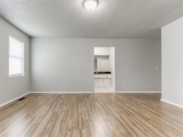 empty room featuring visible vents, a textured ceiling, baseboards, and light wood-style floors