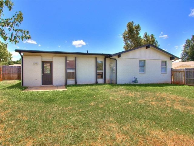 rear view of property featuring a yard, fence, and brick siding