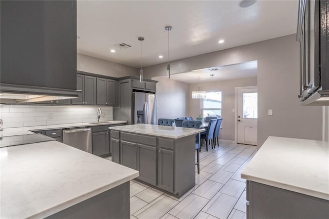 kitchen featuring visible vents, decorative light fixtures, a sink, stainless steel appliances, and backsplash