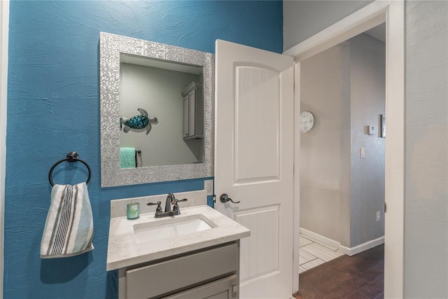 bathroom featuring a textured wall, vanity, baseboards, and wood finished floors