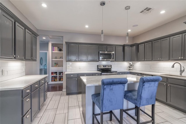 kitchen featuring visible vents, appliances with stainless steel finishes, a sink, a kitchen island, and a kitchen breakfast bar