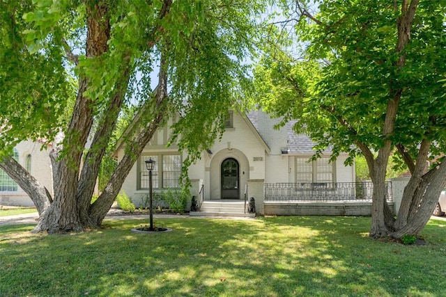 english style home featuring a front lawn, brick siding, and roof with shingles