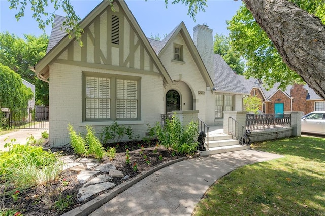 tudor house featuring brick siding, a chimney, a front yard, and a shingled roof