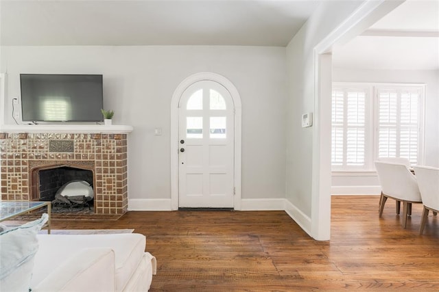 foyer featuring baseboards, plenty of natural light, wood finished floors, and a tiled fireplace