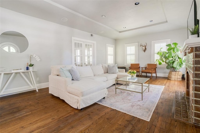 living room featuring a tray ceiling, recessed lighting, wood-type flooring, a stone fireplace, and baseboards