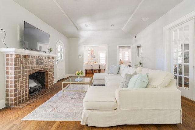 living room featuring a fireplace, baseboards, a tray ceiling, and wood finished floors