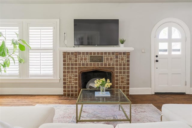 living area featuring a tiled fireplace, wood finished floors, baseboards, and a wealth of natural light