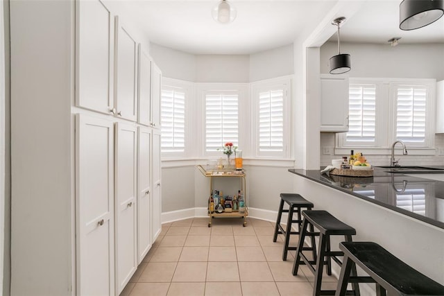 kitchen with dark countertops, a sink, white cabinets, and light tile patterned flooring