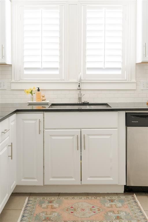 kitchen featuring a sink, stainless steel dishwasher, dark countertops, and white cabinetry