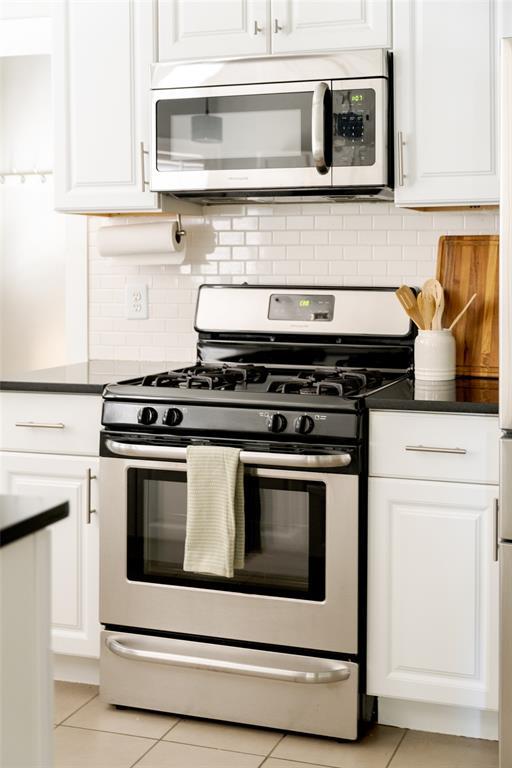 kitchen with light tile patterned floors, stainless steel appliances, white cabinets, dark countertops, and backsplash