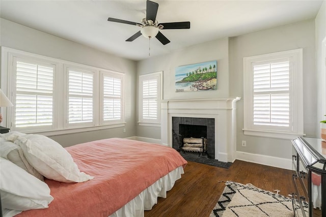 bedroom featuring a tiled fireplace, ceiling fan, baseboards, and wood finished floors