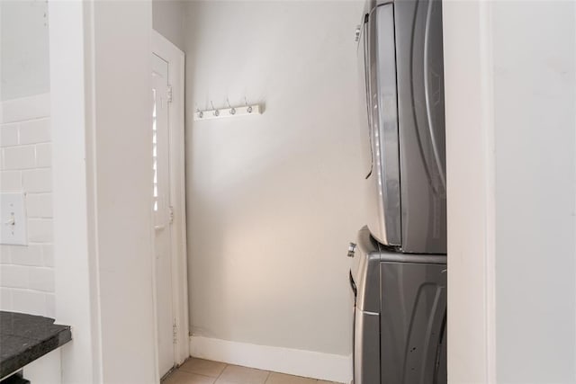 clothes washing area featuring light tile patterned flooring, laundry area, stacked washing maching and dryer, and baseboards