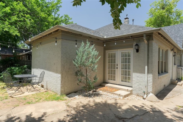 back of property with brick siding, a patio area, french doors, and roof with shingles