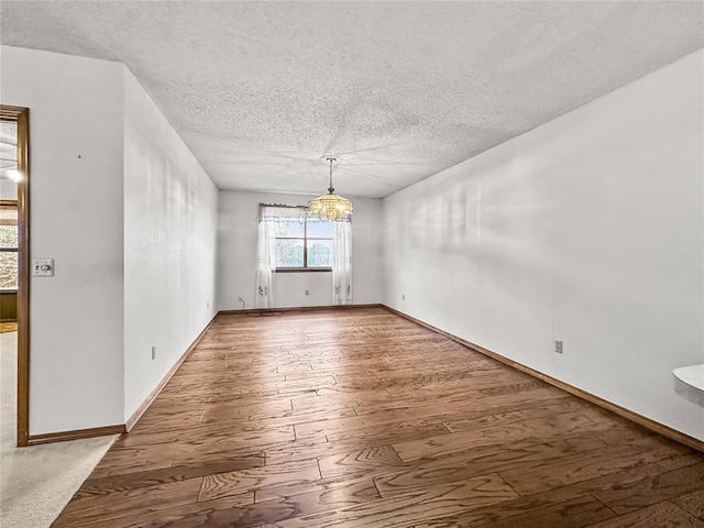 empty room with a notable chandelier, wood-type flooring, and a textured ceiling