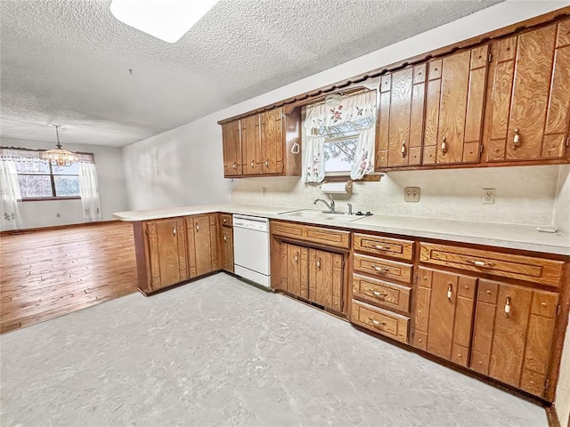 kitchen with sink, white dishwasher, a textured ceiling, decorative light fixtures, and kitchen peninsula