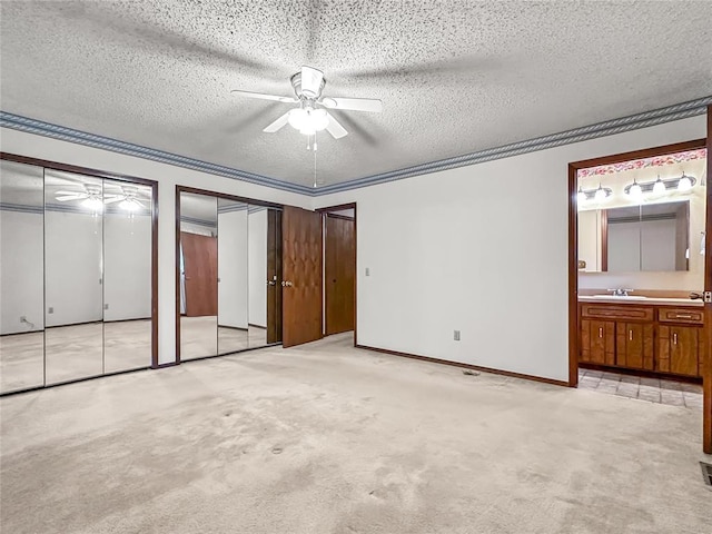 unfurnished bedroom featuring two closets, light colored carpet, ceiling fan, and ensuite bath