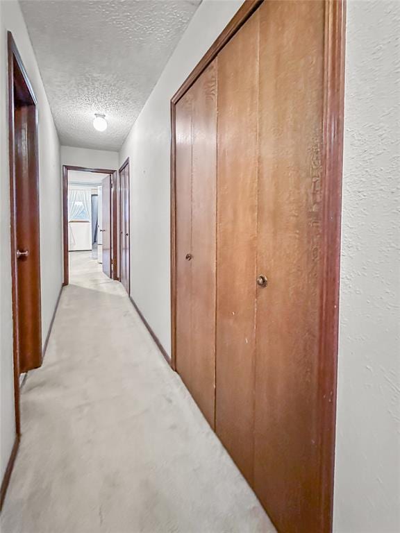 corridor with light carpet and a textured ceiling