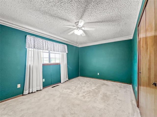 carpeted empty room with a textured ceiling, ornamental molding, and ceiling fan