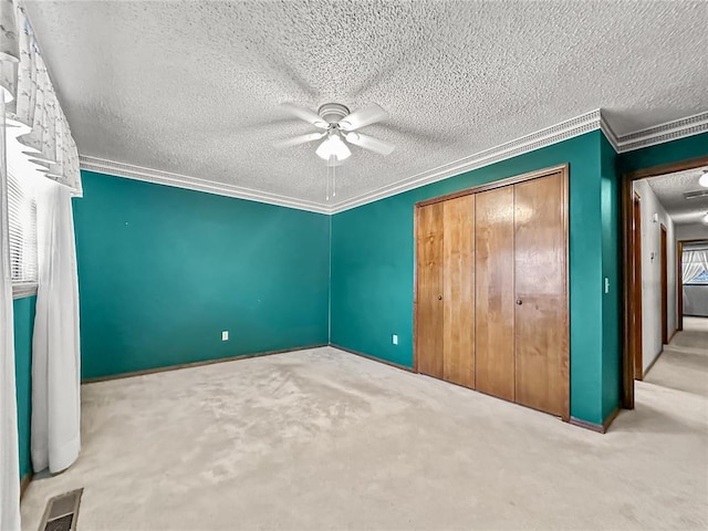 unfurnished bedroom with a textured ceiling, ornamental molding, carpet floors, a closet, and ceiling fan