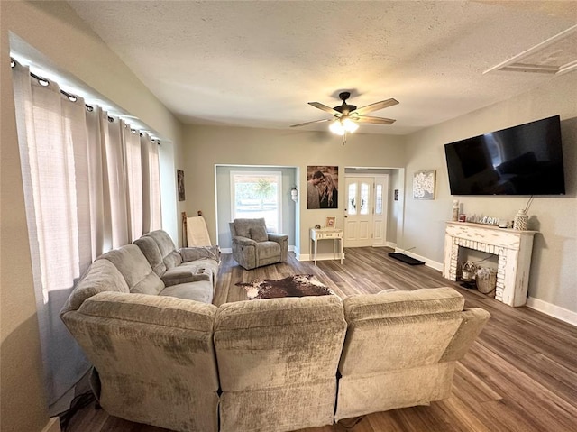 living room featuring ceiling fan, a brick fireplace, hardwood / wood-style floors, and a textured ceiling